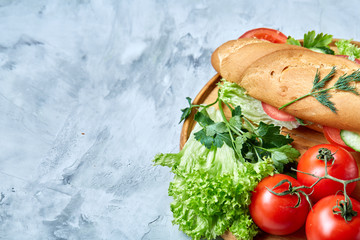 Fresh sandwich with lettuce, tomatoes and cheese served on wooden plate over white textured background, selective focus
