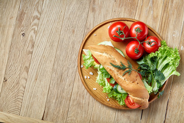 Fresh sandwich with lettuce, tomatoes, cheese on wooden plate, cup of coffee on rustic background, selective focus