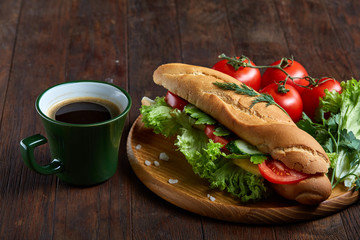 Fresh sandwich with lettuce, tomatoes, cheese on wooden plate, cup of coffee on rustic background, selective focus