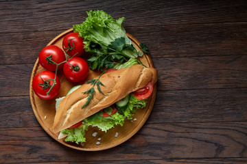 Fresh sandwich with lettuce, tomatoes, cheese on wooden plate, cup of coffee on rustic background, selective focus