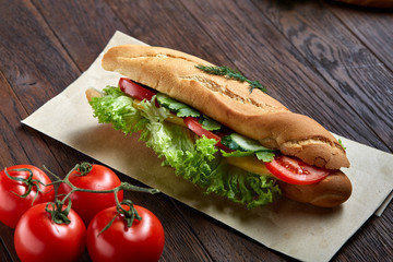 Fresh sandwich with lettuce, tomatoes, cheese on wooden plate, cup of coffee on rustic background, selective focus