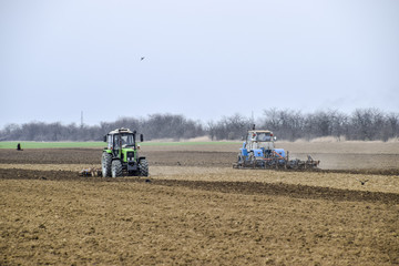 Obraz premium Lush and loosen the soil on the field before sowing. The tractor plows a field with a plow
