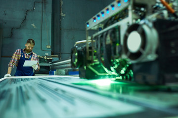 Portrait of young factory worker operating modern laser engraving equipment in industrial workshop,...