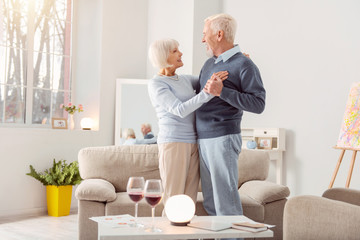 Obraz premium Together forever. Happy elderly couple dancing waltz together in the living room and looking at each other admiringly