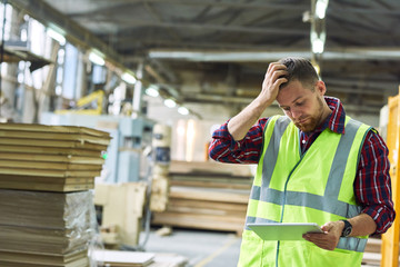 Waist up portrait of young factory worker wearing reflective vest  filling out shipping notice...