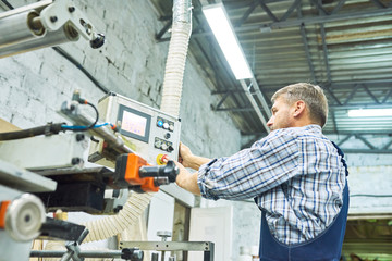 Side view portrait of mature factory worker operating machine unit pressing buttons on control panel, copy space