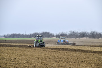 Obraz premium Lush and loosen the soil on the field before sowing. The tractor plows a field with a plow