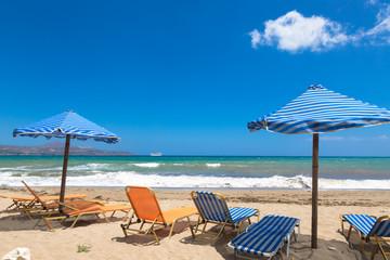 Kalyves sand beach in the island Crete of Greece. Blue umbrellas and deck chairs on background blue sea