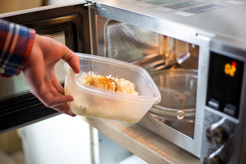Young man hands giving the food into the microwave for warm up