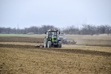 Fototapeta premium Lush and loosen the soil on the field before sowing. The tractor plows a field with a plow
