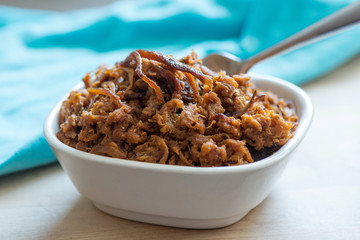 Pulled pork in a white bowl with blue napkin and a fork
