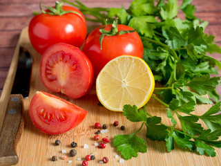 Fresh vegetables Tomatoes Lemon Parsley Pepper coarse Salt and a Knife on a cutting Board