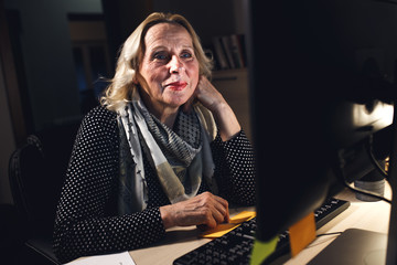 Smiling mature businesswoman working on desktop at night.