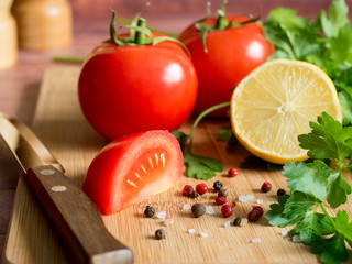 Fresh vegetables Tomatoes Lemon Parsley Pepper coarse Salt and a Knife on a cutting Board