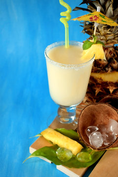 Milk fruit cocktail in an Irish mug decorated with a piece of pineapple, an umbrella and a straw on blue background