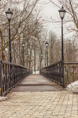 Pedestrian bridge with lanterns, surrounded by trees, winter.