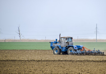 Fototapeta premium Lush and loosen the soil on the field before sowing. The tractor plows a field with a plow
