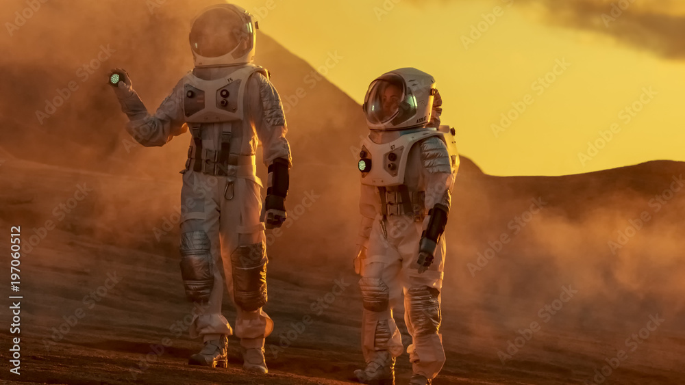 Wall mural two astronauts wearing space suits walk exploring mars/ red planet. space travel and solar system co