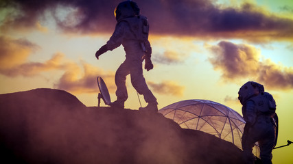 Two Silhouettes of the Astronauts Explore Red Rocky Alien Planet. In the Background Sunset with Base/ Research Station.