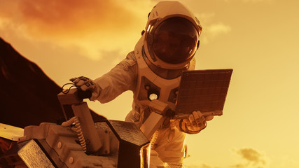 Astronaut in the Space Suit Works on Laptop, Adjusting Rover on a New Alien Red Planet, Presumably...