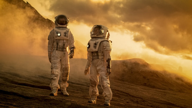 Two Astronauts in Space Suits Confidently Walking on Mars, Exploration Expedition on the Planet's Surface. Red Planet Covered in Rocks, Gas and Smoke. Humans Overcoming Difficulties.