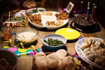 Concept celebration with family and friends. Birthday chocolate cake with arabic food: falafel, hummus, tahini, kibe, pitas and tabbouleh on rustic table. Food background. Middle East cuisine served.
