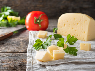 Piece of cheese with parsley, tomatoes on a linen towel Rustic wooden background