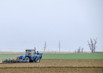 Obraz premium Lush and loosen the soil on the field before sowing. The tractor plows a field with a plow