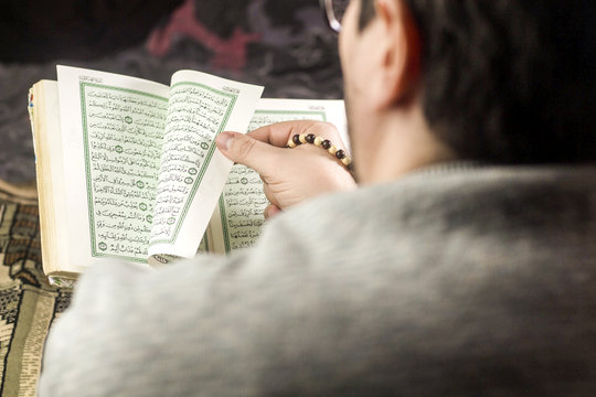 man reading Holly Quran with rosary in his hand