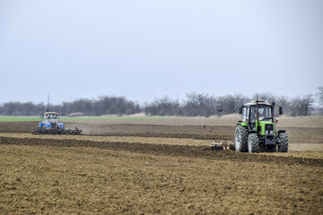 Obraz premium Lush and loosen the soil on the field before sowing. The tractor plows a field with a plow