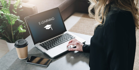 Rear view. Young woman is working on laptop with inscription on screen e-learning and image of...