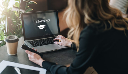 Rear view. Young woman is working on laptop with inscription on screen e-learning and image of...