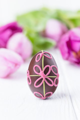 Happy Easter! Chocolate easter egg with pink flowers on a white wooden background