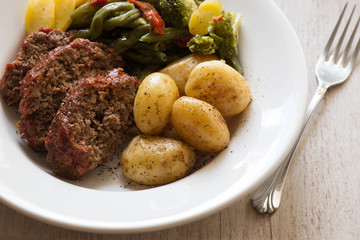 Sliced meatloaf, vegetables and potatoes in a white bowl