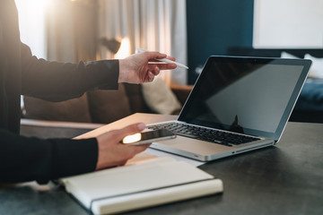 Woman standing near table, pointing pencil on empty screen of laptop. Girl working home on laptop. Online education.