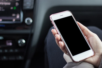 Beautiful woman while sitting on the front passenger seats in the car. Girl is using a smartphone. Hand closeup