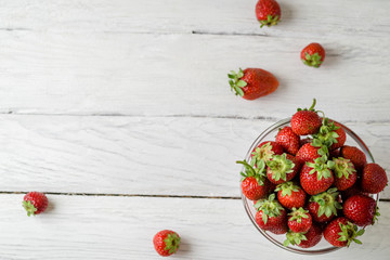 Top view photo of a glass plate with ripe red strawberries on a white wooden table. Four strawberries scattered on a table. Place for text.