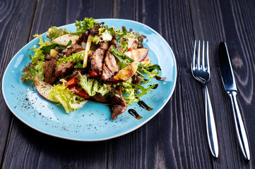 Veal salad with lettuce, apple, pear and tomato on blue plate on dark wooden background, copy space. Restaurant food, close up. Meat salad