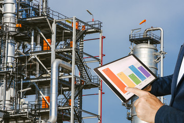 businessman fingers touching chart tablet against oil refinery in petrochemical Aerial view oil refinery night during twilight,Industrial zone,Energy power station 