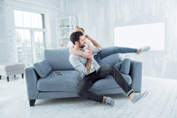 Funny moment. Strong bearded man sitting on the couch and looking aside while joking with his girlfriend