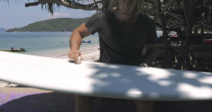 pretty sporty nice guy, man, surfer rubbing his surfboard by wax on sunny beach near ocean, sea (water) in south country or icland