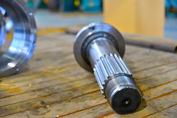 The new splined shaft after machining on the lathe and CNC milling machine lies on a wooden rack in...
