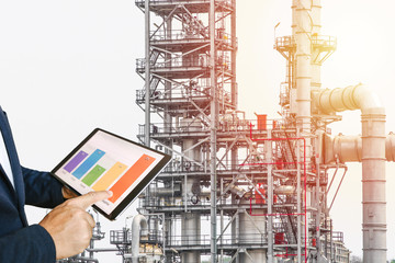 businessman fingers touching chart tablet against oil refinery in petrochemical Aerial view oil refinery night during twilight,Industrial zone,Energy power station 