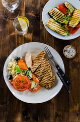 Grilled chicken breast with tabbouleh salad and grilled vegetables on dark wooden background