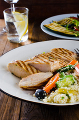 Grilled chicken breast with tabbouleh salad and grilled vegetables on dark wooden background