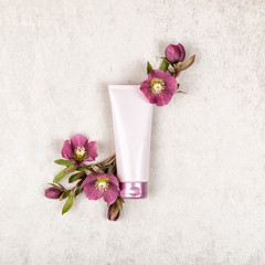 Pink cosmetic product layout with red flowers on rustic stone shabby chic beige background. Luxury beauty concept with tube of cream, top view, flat lay and copy space