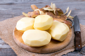 Peeled potatoes with the peel and knife on a wooden table