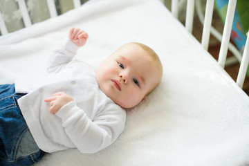 Funny baby in white crib with canopy. Nursery interior and bedding for kids. Laughing little boy playing. Bedroom for young children. Happy child in white pajamas.