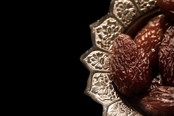 Close-up portrait of dates which are a traditional food to break fast during the holy month of ramadan on a silver serving platter with a black background. Dubai, UAE.