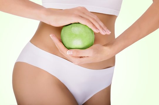 woman dressed in white underwear, holding a green apple in her hands, close-up. concept of diet and the ideal body